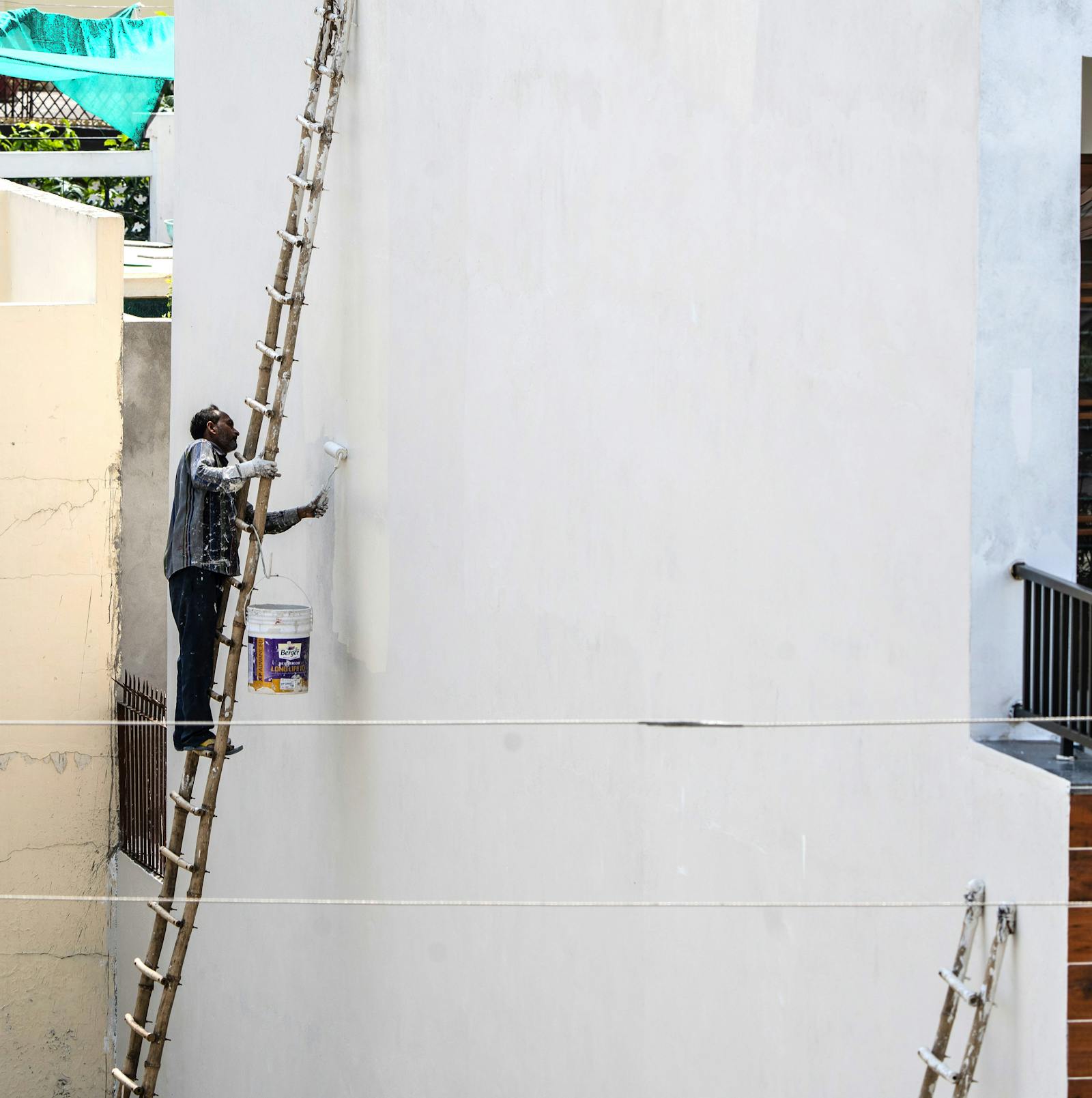 Painter on a ladder painting a high exterior wall