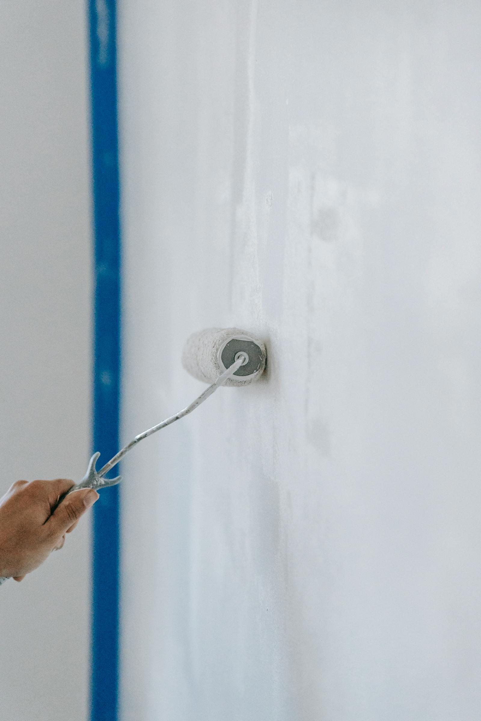 Close-up of a roller applying white paint to an interior wall